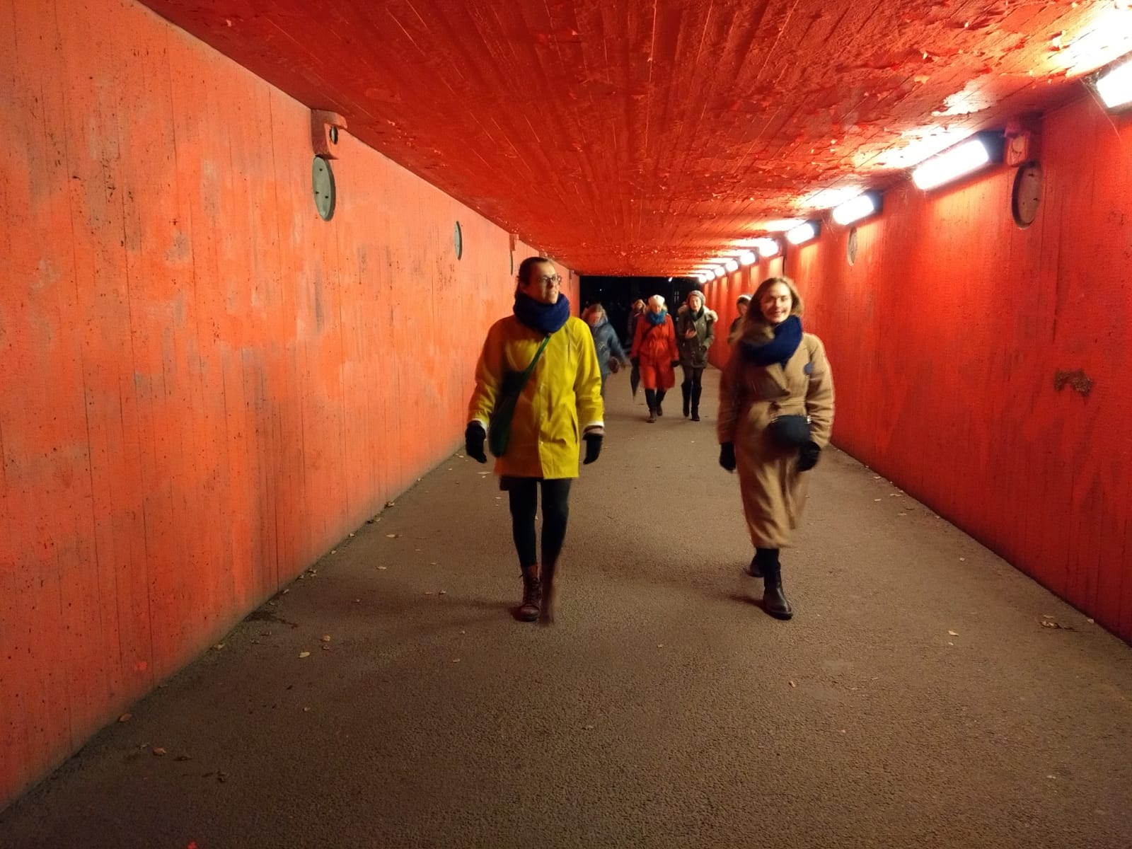 people walking towards the camera inside an underground tunnel that's painted red
